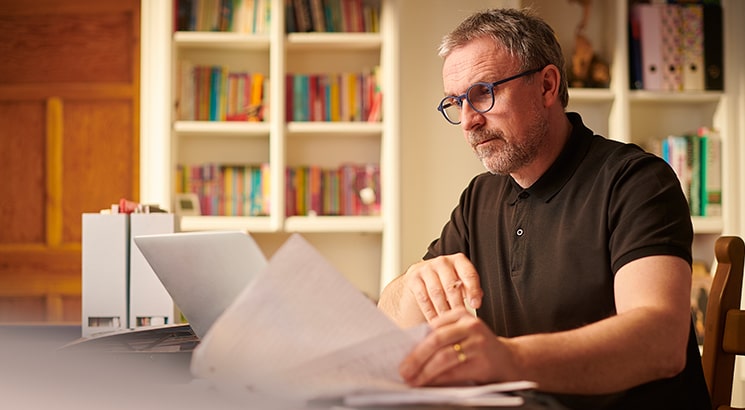 A man sits in his living room looking over paperwork